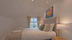 Un dormitorio con cama, una mesita de noche, una lámpara, un cuadro y una ventana con cortinas.