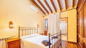 Quarto com cama, mesa de cabeceira, chão de madeira e janela com cortinas.