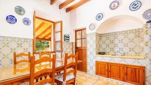 Uma área de refeições com mesa e cadeiras de madeira, uma cozinha com painel de azulejos e uma janela com vista para o verde.
