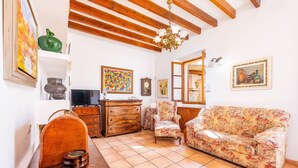 Sala de estar com teto de madeira, sofá, poltrona, televisão e diversos objetos de decoração nas paredes.