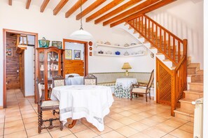 Un comedor con una mesa dispuesta para dos personas, una escalera de madera y una estantería con vajilla.