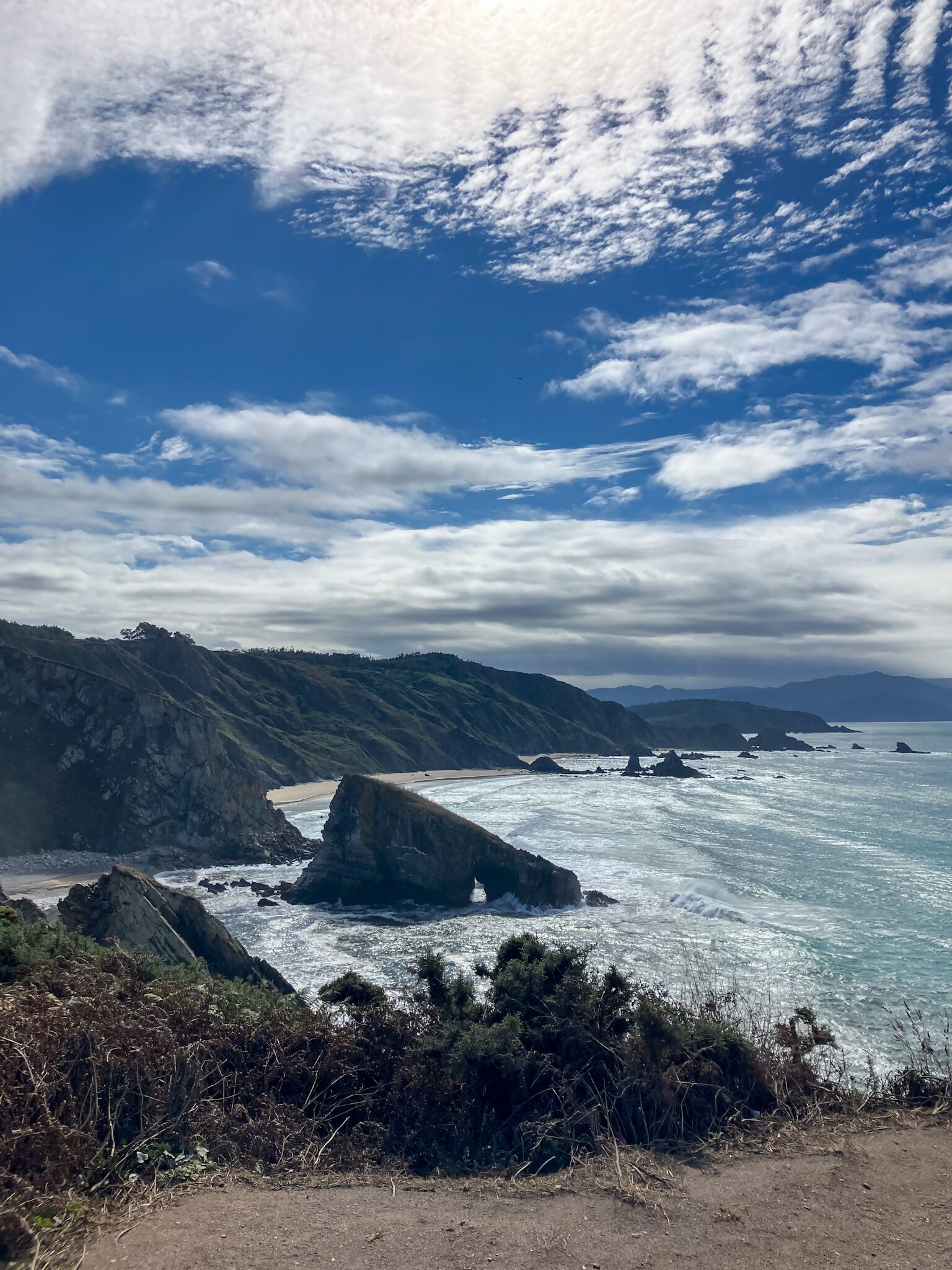 Un paysage côtier caractérisé par des falaises rocheuses, une plage de sable et un ciel dégagé.