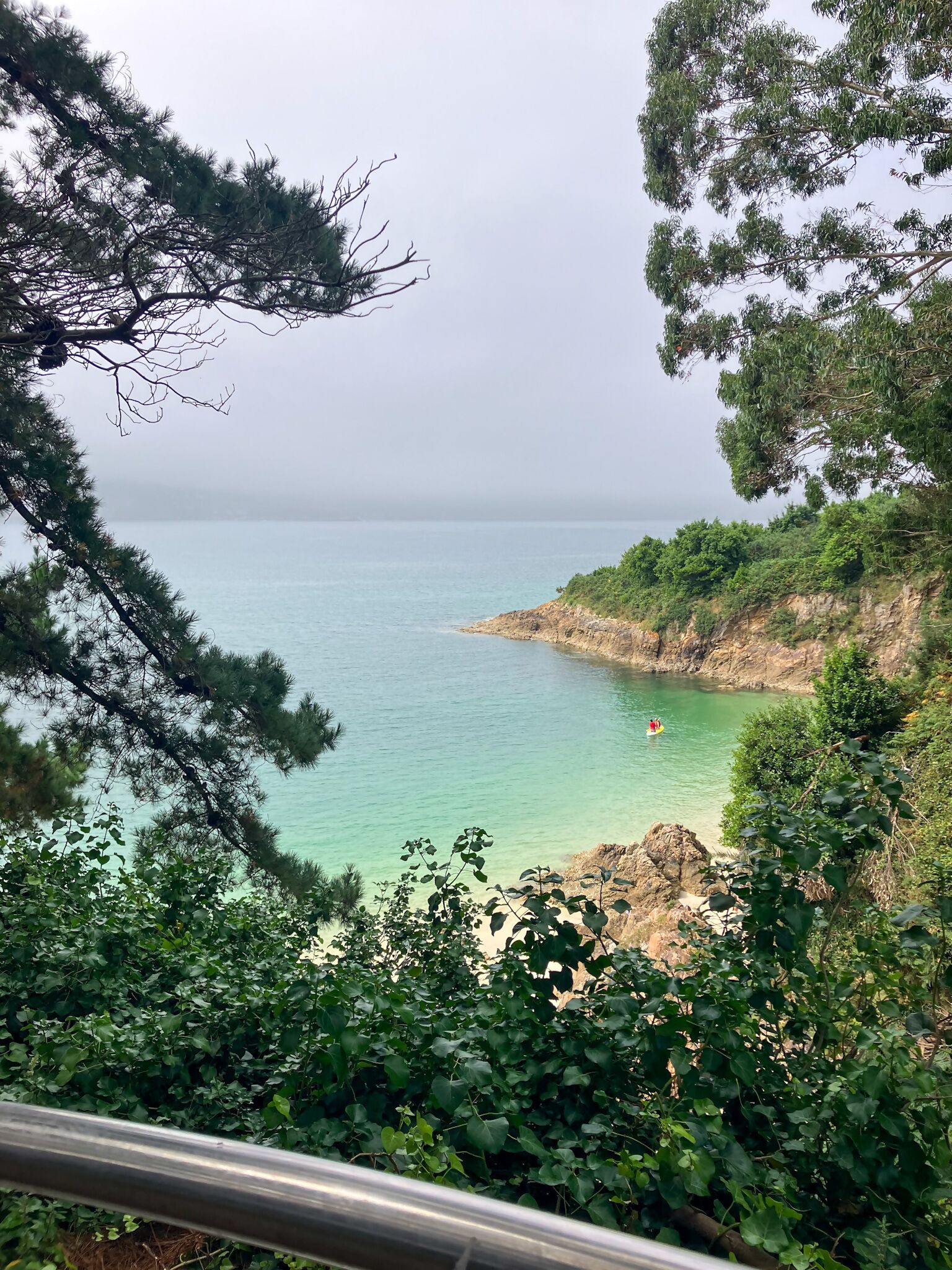 A coastal landscape with clear turquoise water, rocky cliffs, and dense greenery.