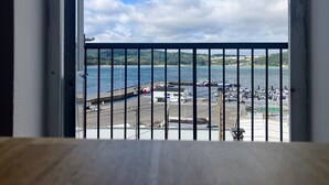 Vista des d'un balcó sobre un port esportiu amb vaixells amarrats, un moll i un paisatge amb muntanyes a la distància.