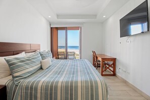 Une chambre avec un lit, une télévision, un bureau et une vue sur la plage.