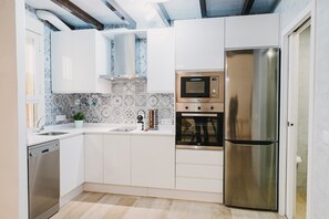 Una cocina moderna con armarios blancos, un refrigerador de acero inoxidable, un horno integrado y un microondas.