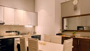 A modern kitchen with white cabinets, a dining table with chairs, and a clock on the wall. - 2 Bedroom Apartment in Colombo 05 (Colombo)