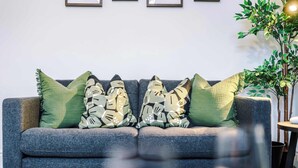 Um sofá cinzento com almofadas estampadas, uma mesinha e um vaso com planta.