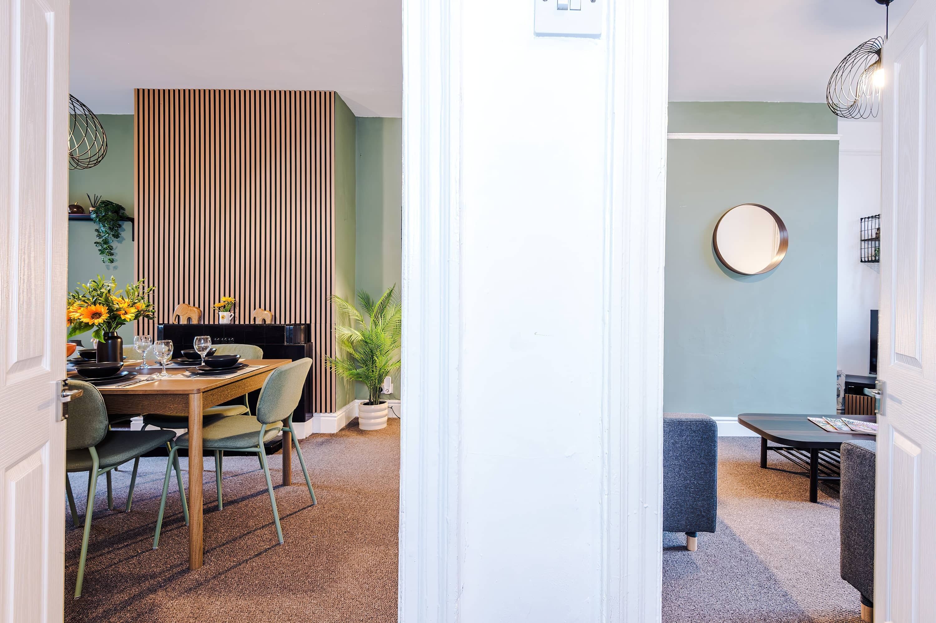 A dining area with a wooden table, chairs, and a striped partition. There is a potted plant and a mirror on the wall.