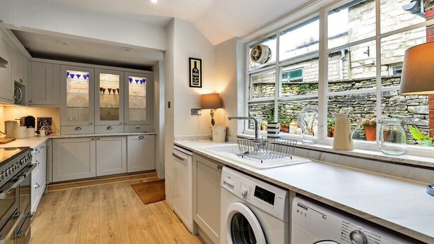 Une cuisine moderne avec des meubles gris, un lave-linge encastré et une fenêtre donnant sur un mur en pierre et de la verdure.