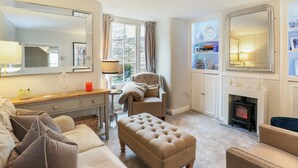 Un salon chaleureux avec un canapé, un pouf et un fauteuil, une cheminée et un grand miroir.