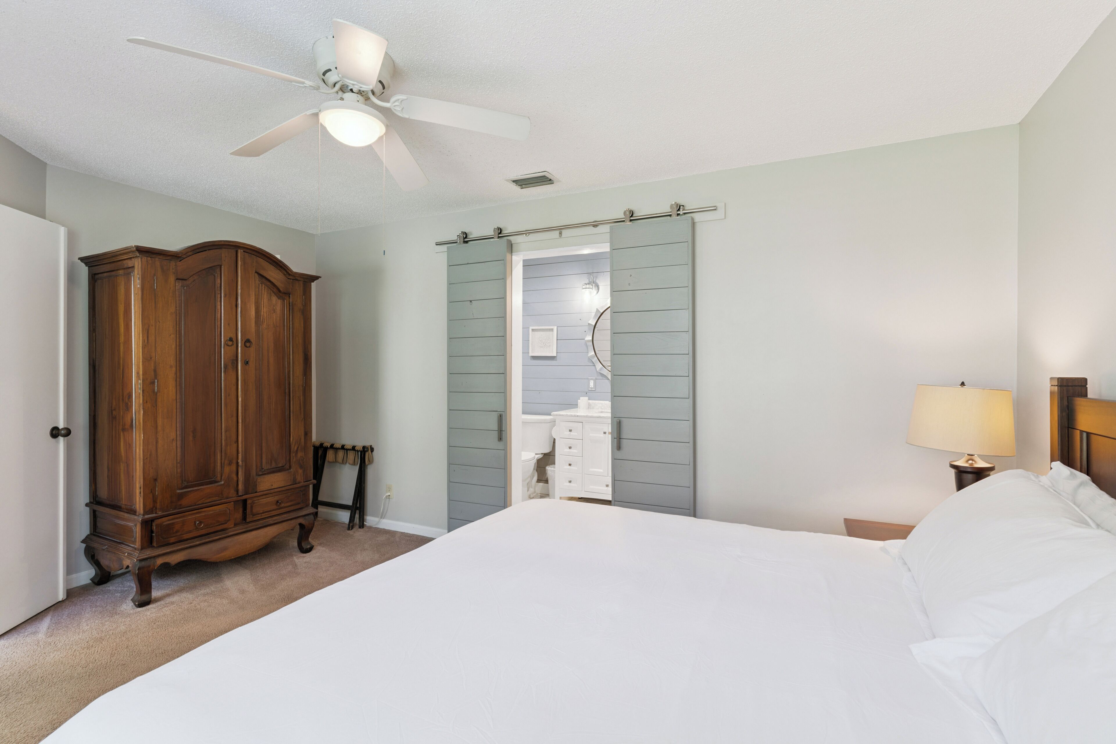 Een slaapkamer met een bed, een kledingkast, een badkamer zichtbaar door een deur en een plafondventilator.