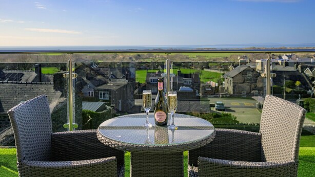 A wicker table with two glasses of champagne and a bottle, overlooking a village with stone buildings. - Tan-Y-Foel (Dyffryn Ardudwy)