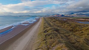 A coastal landscape with a beach, grassy terrain, and distant mountains under a partly cloudy sky. - Tan-Y-Foel (Dyffryn Ardudwy)