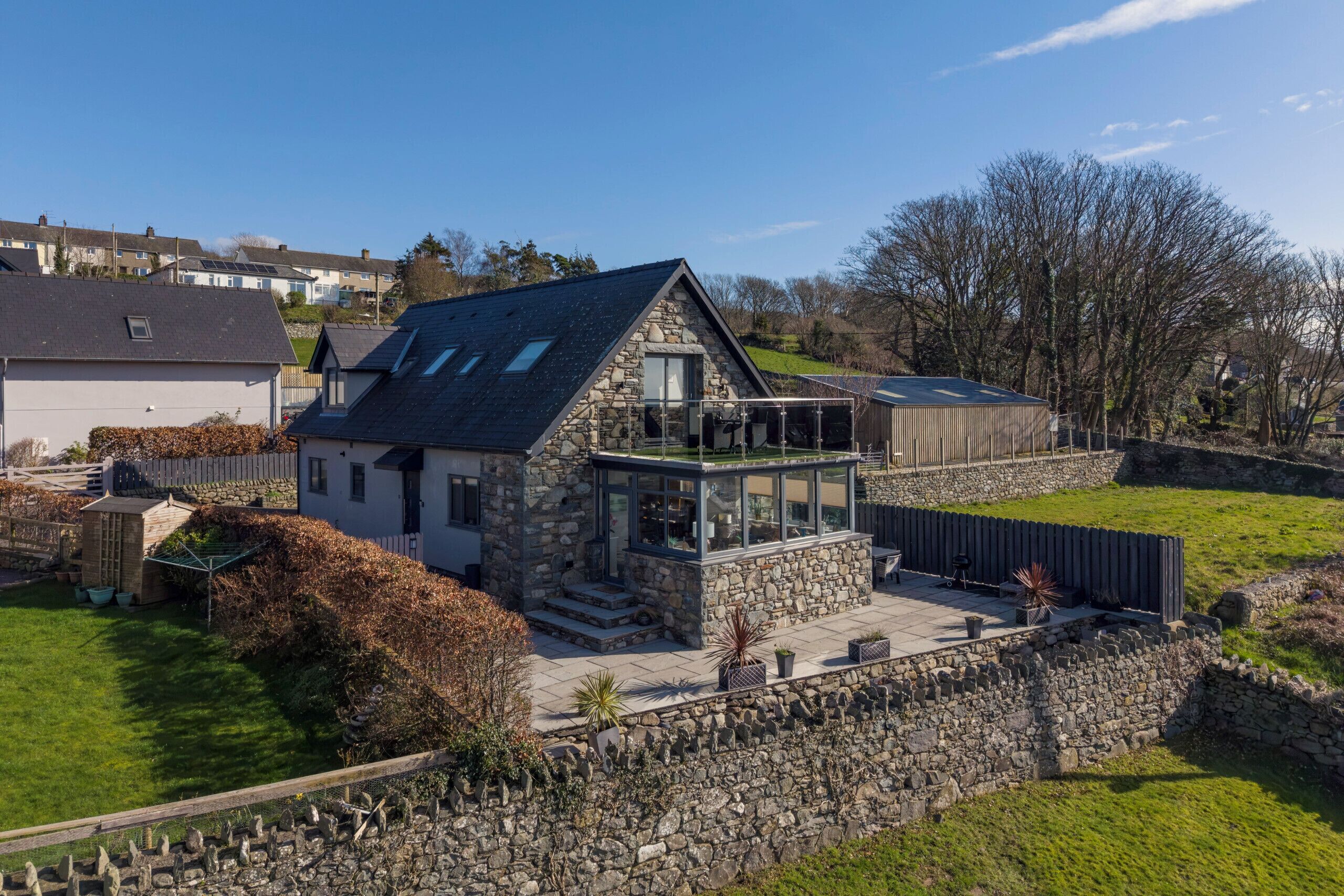 Une maison en pierre avec un balcon, une cour clôturée et un ciel dégagé.