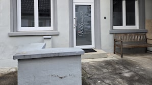 Une façade d’immeuble avec deux fenêtres, une porte sur laquelle est affiché un panneau d’accueil et un banc à l’extérieur.