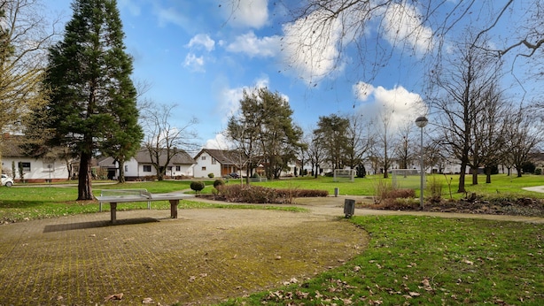 Un parc doté d’une zone dallée, de bancs et d’arbres.