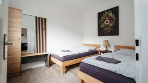 Une chambre avec deux lits en bois, un miroir, une horloge et une œuvre d’art accrochée au mur.