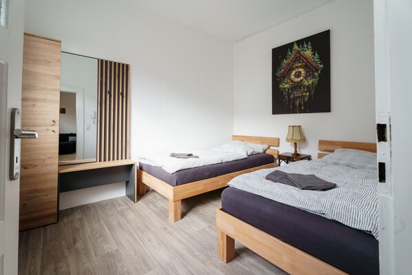 Ein Zimmer mit zwei Holzbett, einem Spiegel, einer Uhr und einem Wandbild.