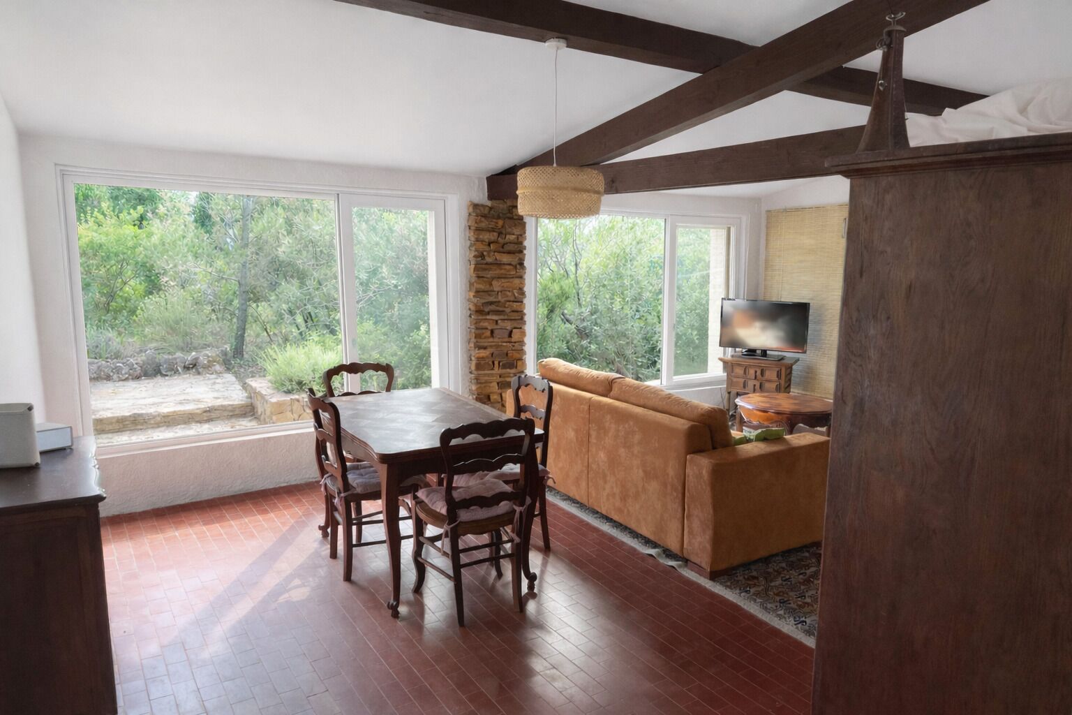 A dining area with a wooden table and chairs, a stone wall, and a television on a wooden stand.