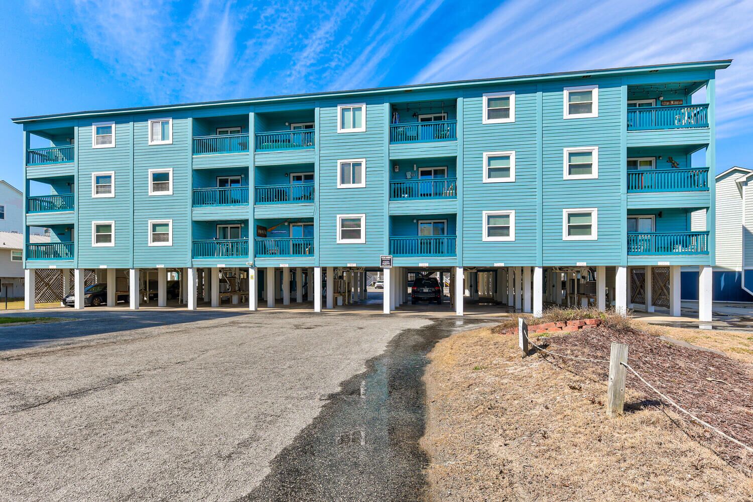 A multi-story building with balconies and a parking area in front.