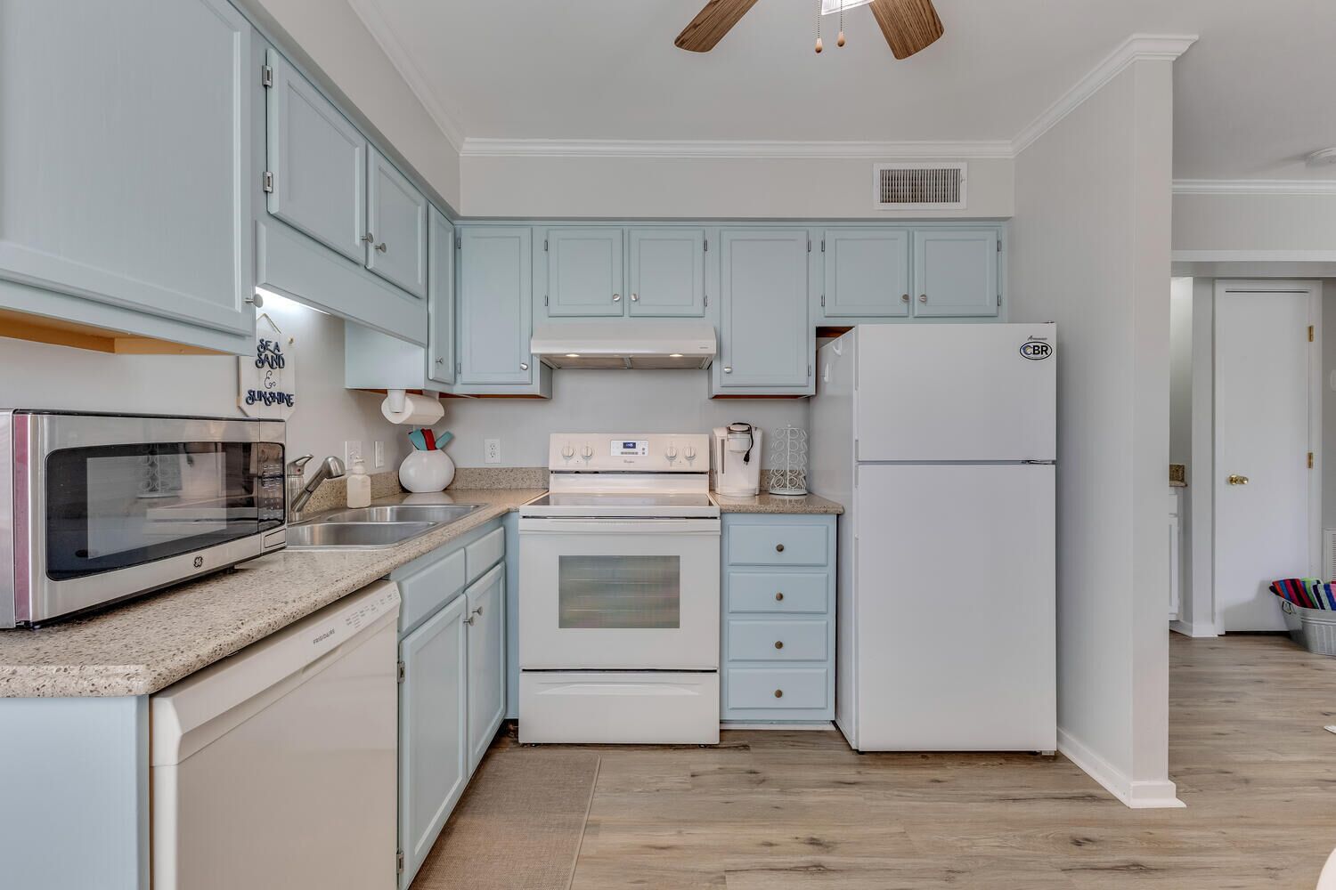 A kitchen with light blue cabinets, a stainless steel microwave, a white stove, and a white refrigerator.