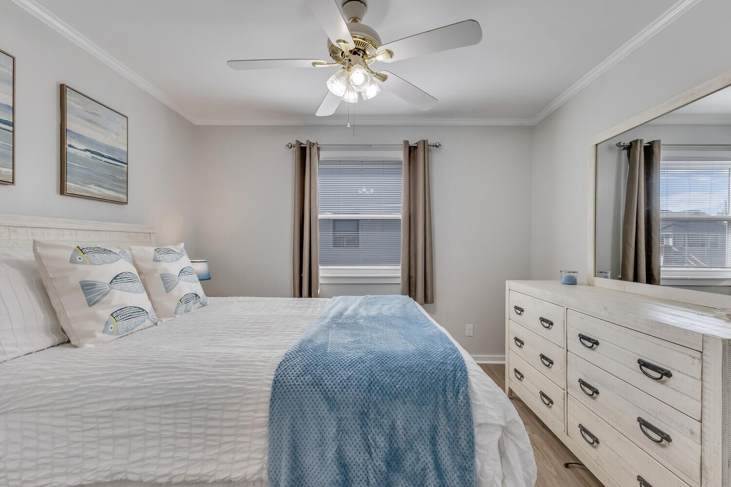 Une chambre à coucher avec un lit, une commode, un ventilateur de plafond et une fenêtre avec des rideaux.