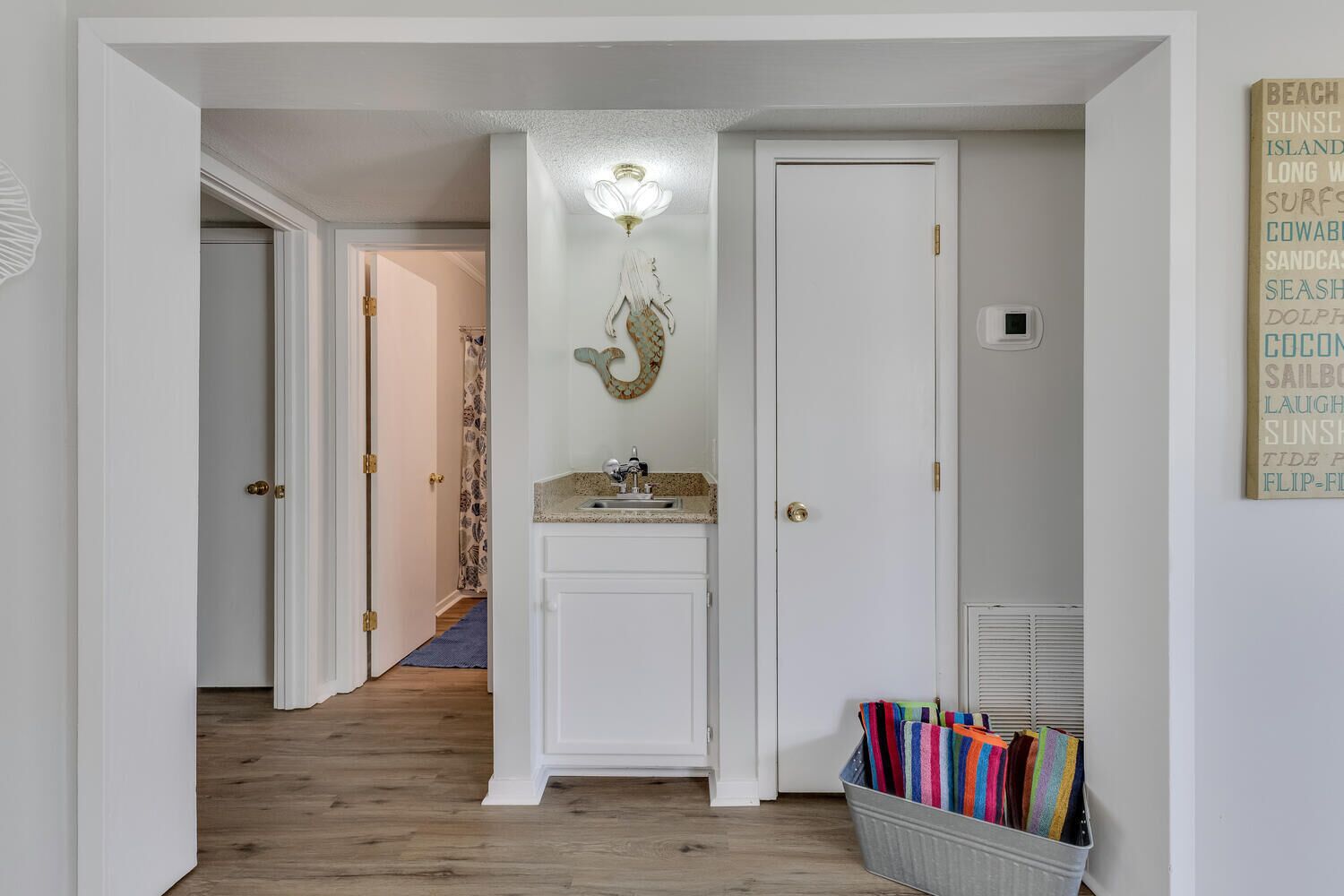 A hallway with a white door, a wall-mounted light fixture, a small sink, and a basket of colorful towels.