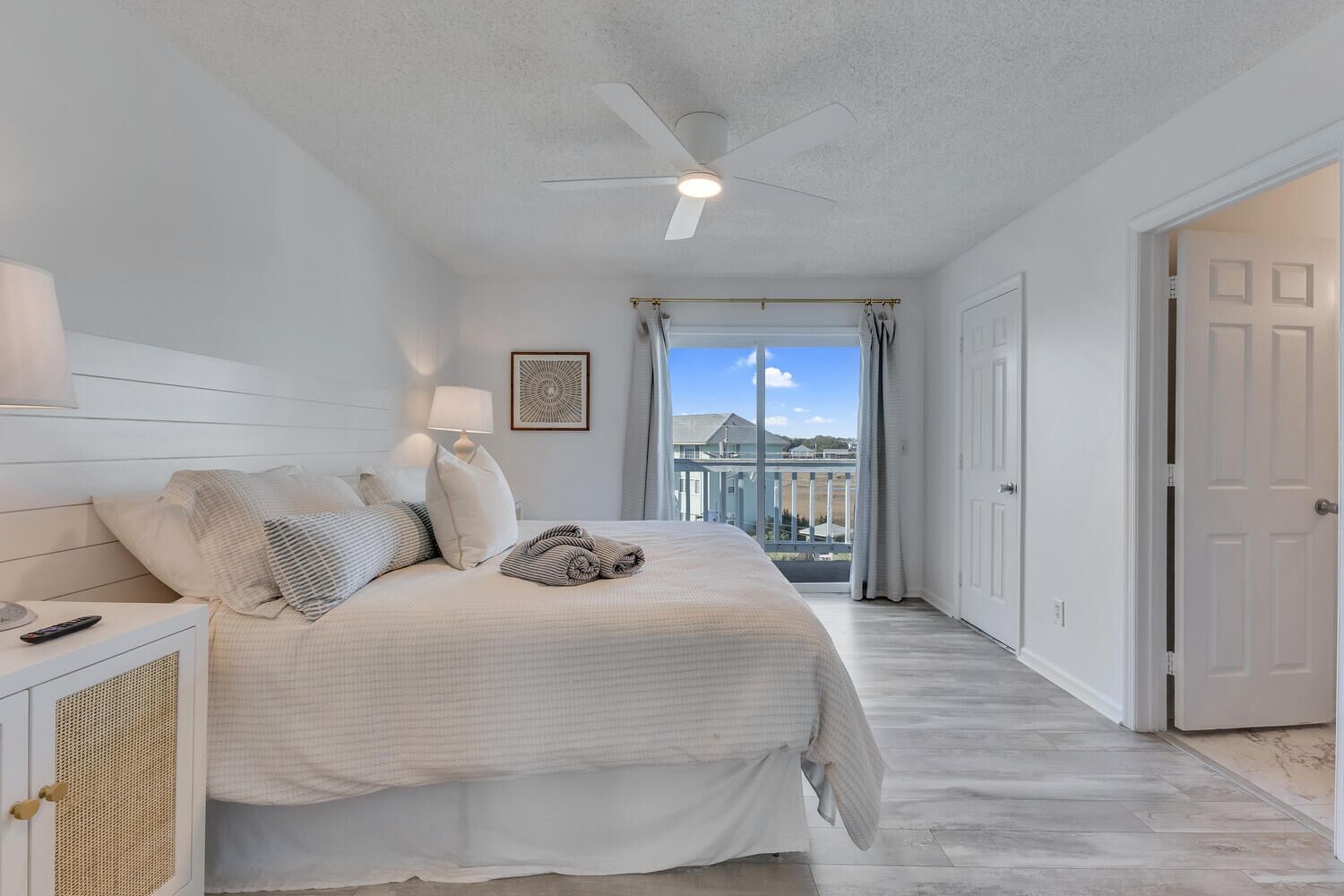 A bedroom with a bed, bedside tables, a ceiling fan, and a view of the outside.