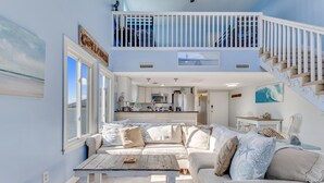 A spacious living area with a large sofa, a coffee table, and a view of the kitchen and balcony. - Paradise Tides - 6 Bedroom Duplex with Community Pool (Carolina)