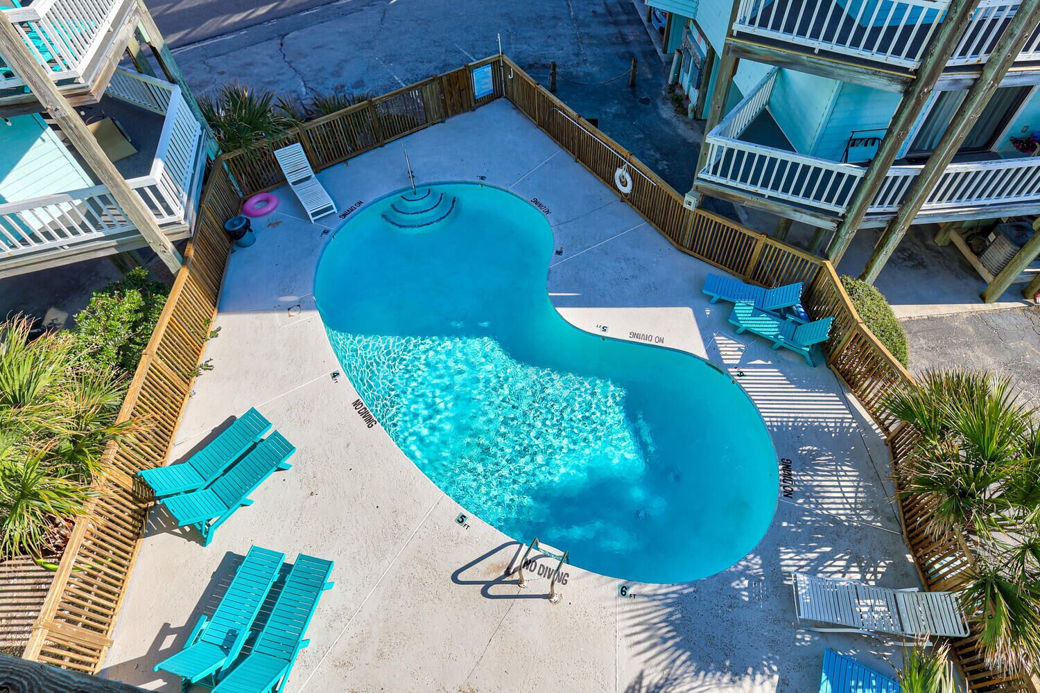 Una piscina de forma peculiar, con forma de riñón, rodeada de vallas de madera y sillas reclinables azules.