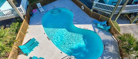 Una piscina de forma peculiar, con forma de riñón, rodeada de vallas de madera y sillas reclinables azules.
