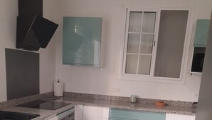 Moderni keittiö, jossa on graniittitaso, valkoiset ja turkoosit kaapit, sisäänrakennettu uuni ja ikkuna, jossa on himmeä lasi.