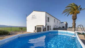 Una piscina con un edificio blanco que muestra la leyenda 'MASIA Clambrich' al fondo.