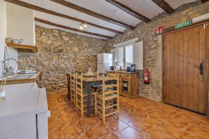 Une cuisine rustique avec des murs en pierre, des poutres en bois, un sol carrelé et une porte en bois portant l’inscription « SORTIDA ».