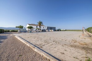 A large open concrete area with a white building, a palm tree, and a green tractor.