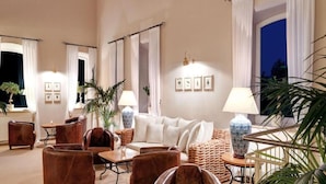Ein großzügiger Lounge-Bereich mit Ledersesseln, einem weißen Sofa und einem Couchtisch. Ücht Blumentöpfe und eine Lampe stehen auf einem Beistelltisch.
