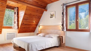 A bedroom with a sloped ceiling, a bed, a nightstand, a window with a view of trees, and a picture on the wall. - Holiday Home 'Gite 8 Personnes, Val D'azun' with Mountain View, Private Terrace and Wi-Fi (Bun)