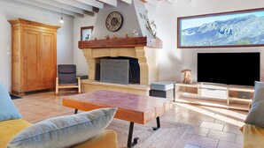 A living room with a fireplace, wooden furniture, a television, and a stone fireplace surround. - Holiday Home 'Gite 8 Personnes, Val D'azun' with Mountain View, Private Terrace and Wi-Fi (Bun)