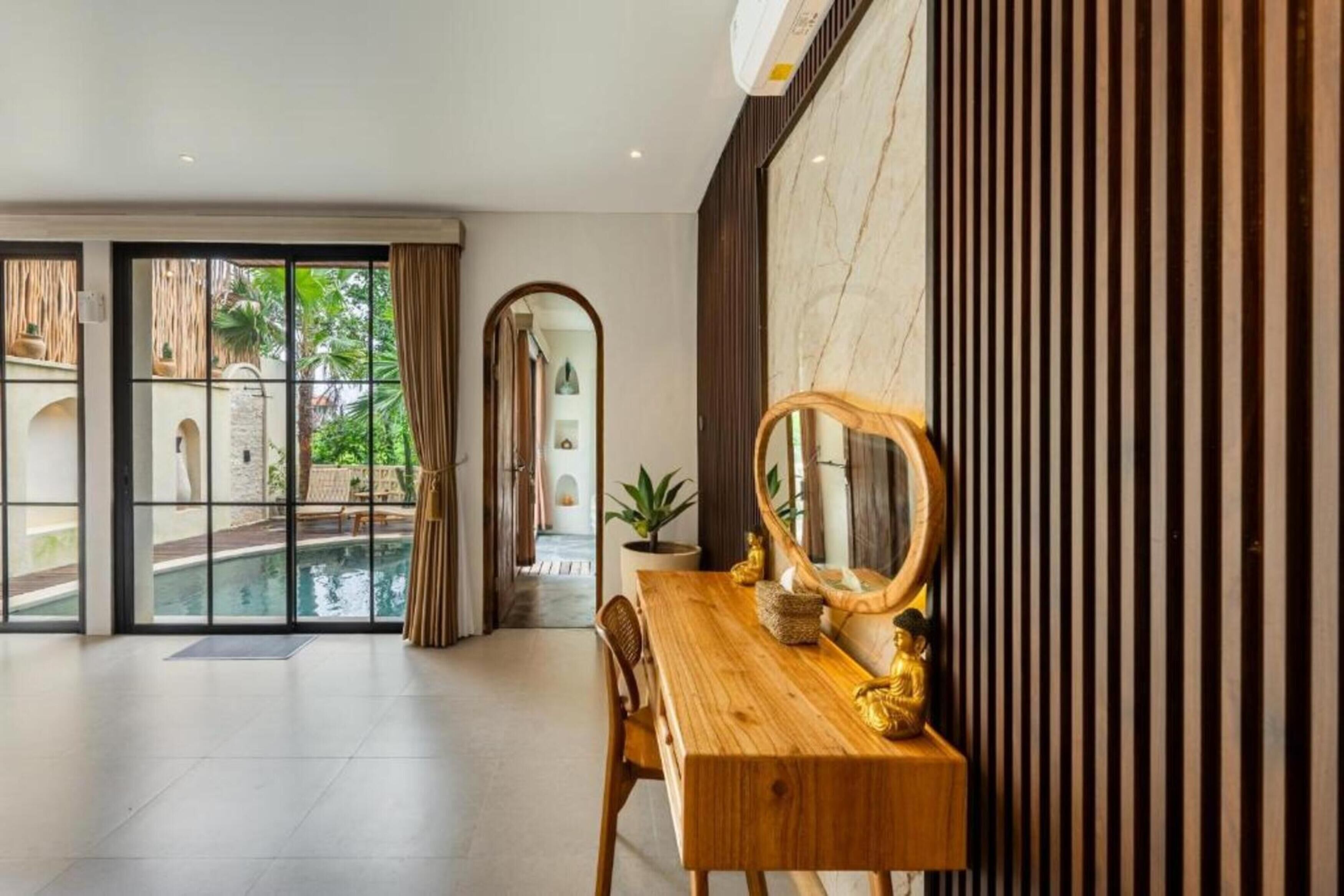 A modern hotel room with a wooden desk, a large mirror, and a view of a swimming pool.