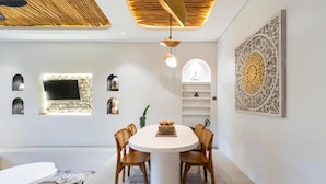 A modern dining area with a round table, wooden chairs, and a white ceiling with a wooden design. - Maha Villa Ubud  (Sukawati)
