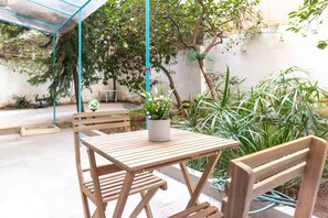 A wooden table and chairs under a blue canopy, surrounded by potted plants and a tree. - A Haven in Kypseli A Basement Apartment (Athens)