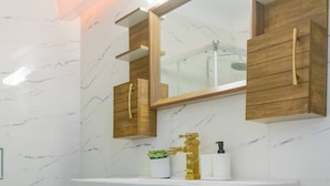 Un baño con pared de mármol, tocador de madera y un espejo grande.
