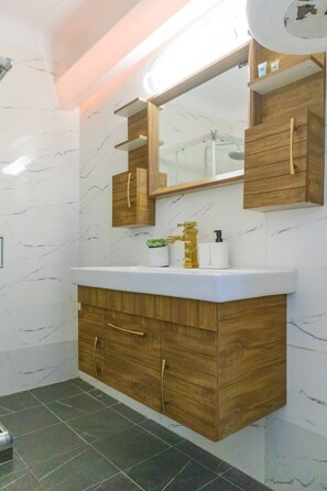 A bathroom with a marble wall, wooden vanity, and a large mirror. - A Haven in Kypseli A Basement Apartment (Athens)