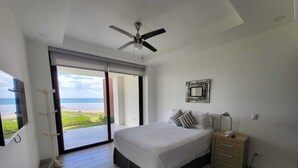 A bedroom with a bed, a nightstand, a ceiling fan, and a view of the ocean through a sliding door. - Hacienda Iguana Beachfront 2BR Poolside- Costamar (Tola)