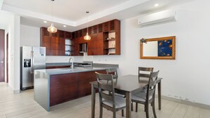 A modern kitchen with a central island, wooden cabinets, and a dining area with chairs. - Hacienda Iguana Beachfront 2BR Poolside- Costamar (Tola)