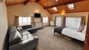 A spacious bedroom with a large bed, a sofa, a dresser, and a TV mounted on the wall. - Deandale Stays (Wilmslow)