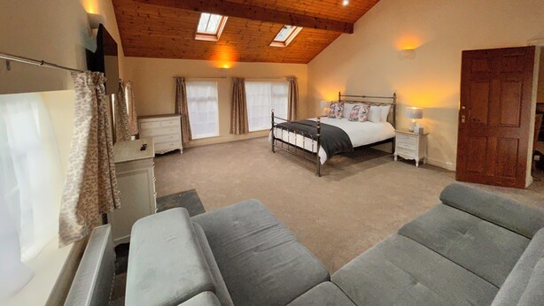 A bedroom with a sloped ceiling, a bed, a nightstand, a dresser, and a window with curtains. - Deandale Stays (Wilmslow)