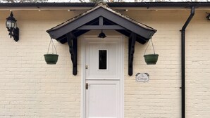 A white door with a black roof and a welcome mat at the entrance. - Deandale Stays (Wilmslow)
