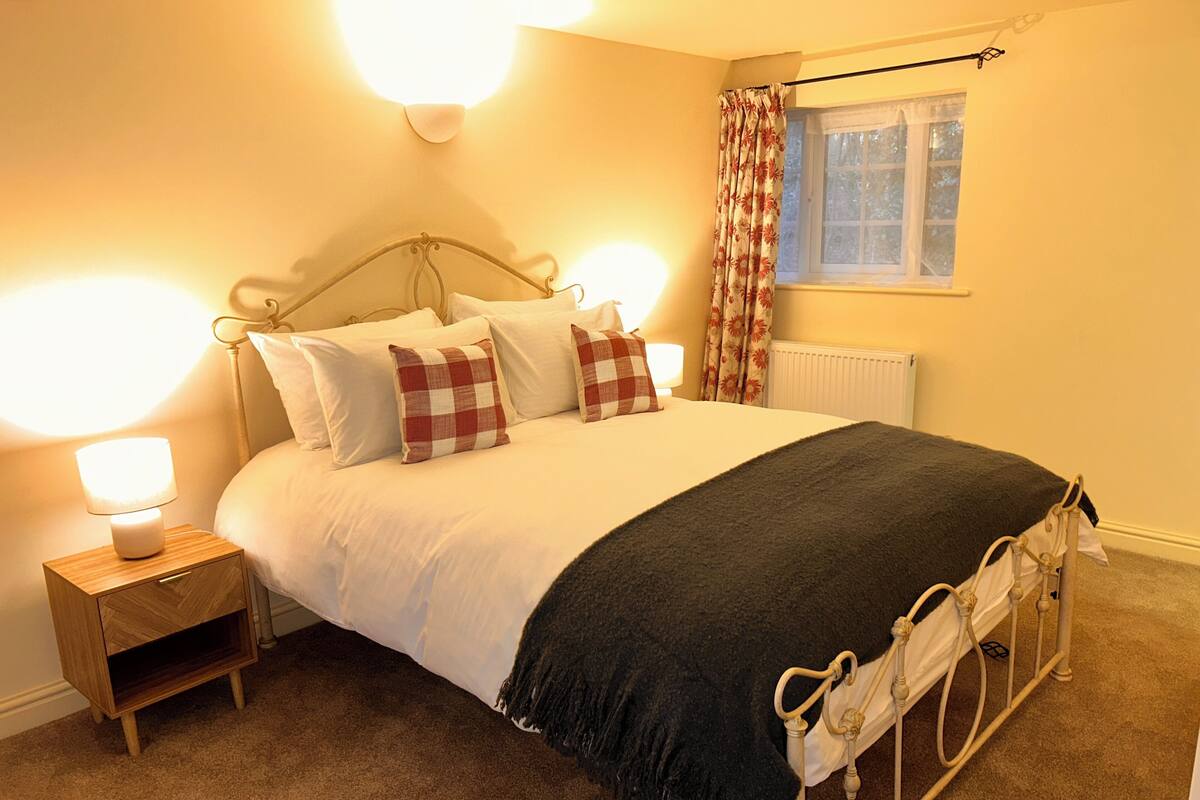A bedroom with a bed, bedside tables, a lamp, a radiator, and a window with curtains.